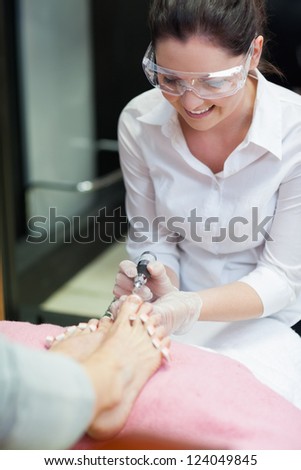 Nail technician removing callus at feet in nail salon