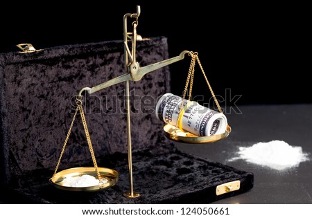 Weighing scales with wad of dollars and white powdered drug beside big pile of drug