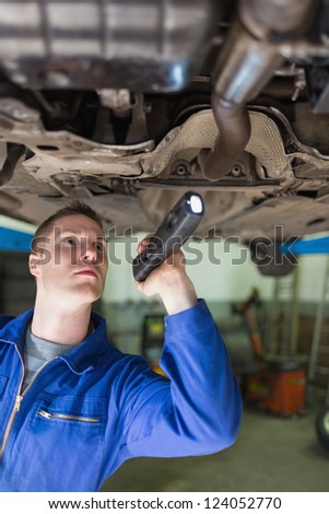 Male mechanic with flashlight examining under car