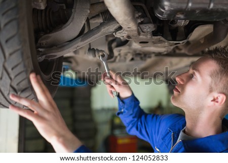 Male auto mechanic working under car in garage