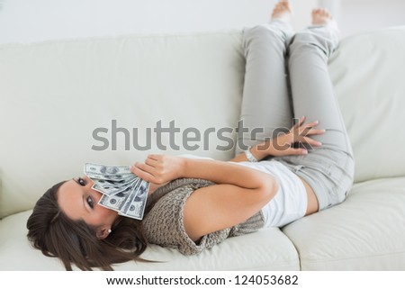 Woman lying on sofa and smelling dollars in the living room with her feet up