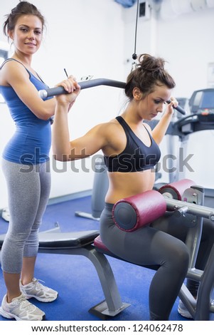 Female trainer with client on weights machine in gym