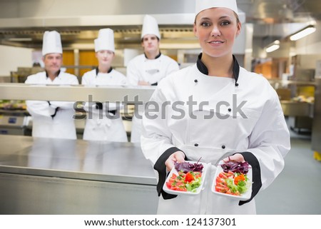 Smiling chef looking presenting salads in the kitchen with team standing behind
