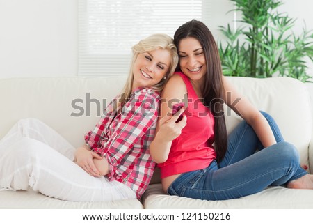 Women sitting back to back on the couch smiling and looking at mobile phone