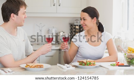 Two people clinking glasses for drinking and eating sandwiches in the kitchen