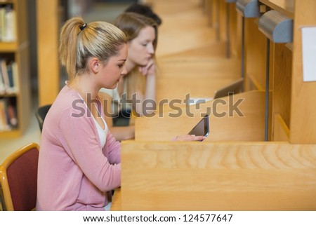 Woman using tablet pc to study at desks in college library