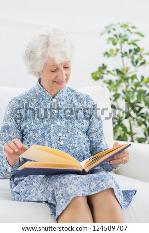 Elderly happy woman looking at her family album on a sofa