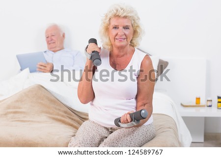 Elderly woman exercising with hand weights sitting on the bed