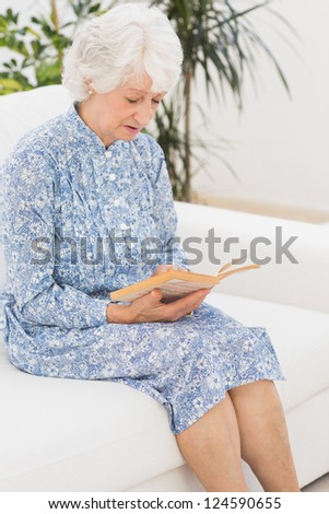 Elderly calm woman reading a old novel on a sofa
