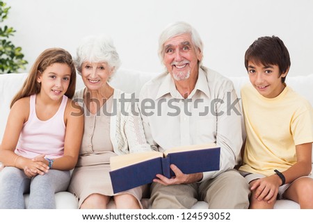 Smiling grandparents with grandchildren reading book on couch