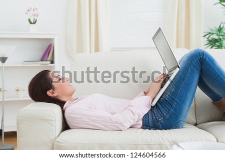 Side view of casual happy woman lying on sofa and using laptop