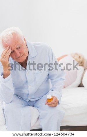 Old man having a headache while woman sleeping on the bed