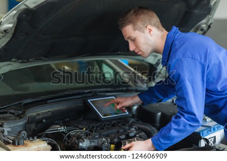 Male mechanic using tablet pc while examining car engine