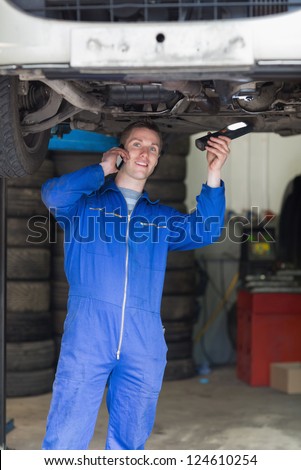 Portrait of auto mechanic using cell phone as he stands under car
