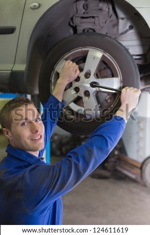 Portrait of male mechanic fixing car tire with wrench in garage