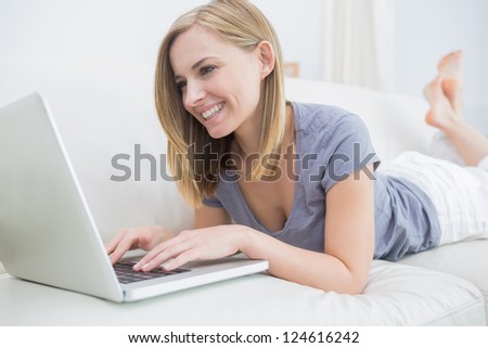 Casual young woman lying on couch and using laptop at home
