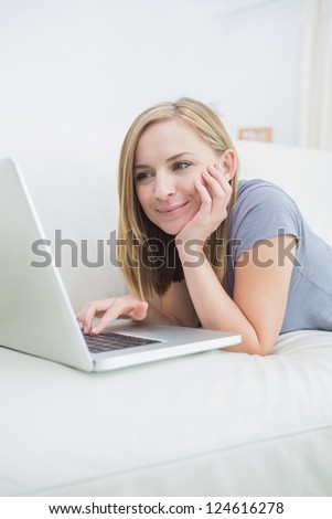 Casual young woman lying on couch and using laptop at home
