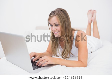 Joyful woman typing on the laptop lying on her bed  in the white bedroom