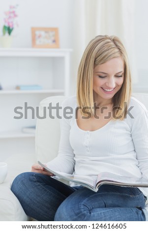 Happy casual young woman reading magazine on couch at home