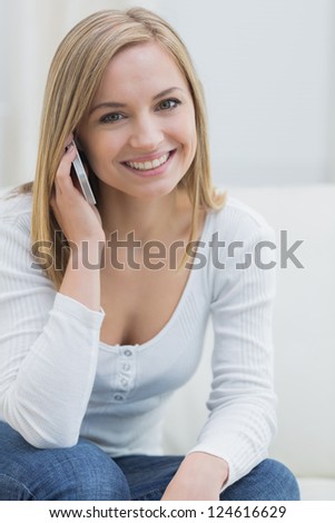 Portrait of casual young woman using mobile phone while sitting on couch at home