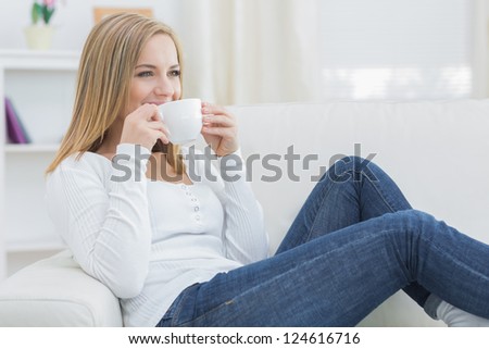 Young woman drinking coffee as she looks away on couch at home