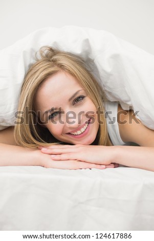 Close-up portrait of beautiful young woman under sheet in bed at home