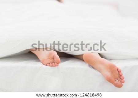 Woman\'s feet sticking out of blanket on bed at home