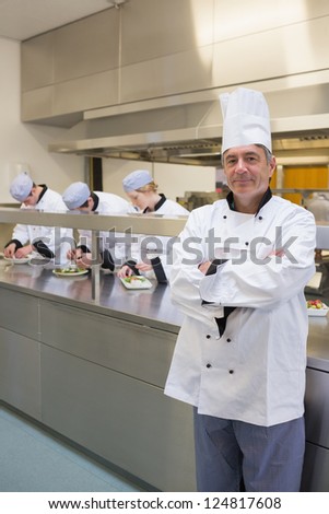 Head chef standing and smiling with his team working behind him in the kitchen