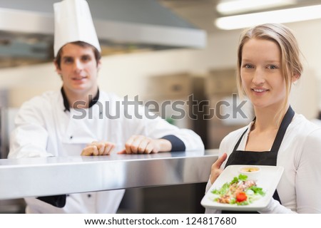 Waitress holding salmon dish smiling with chef in the kitchen