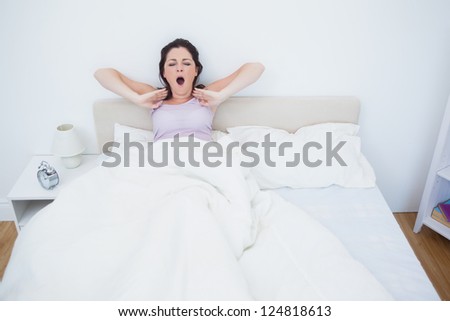 Sleepy young woman sitting and yawning in bed