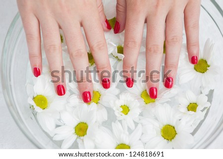 Close-up of red painted finger nails and bowl of flowers at hands spa