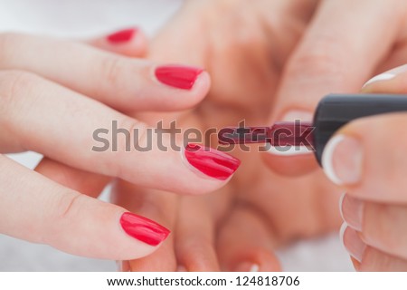 Details shot of hands applying red nail varnish to finger nails at nail salon