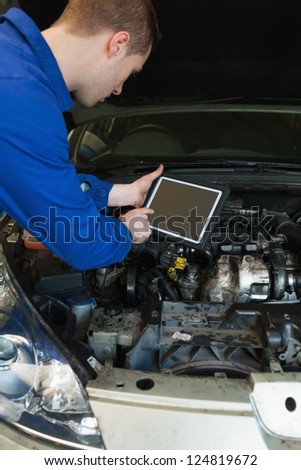 Male mechanic by car with open hood using tablet computer