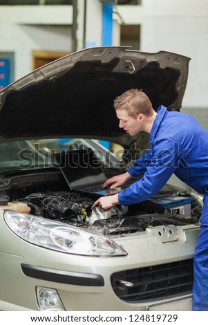 Auto mechanic with laptop repairing car engine in workshop