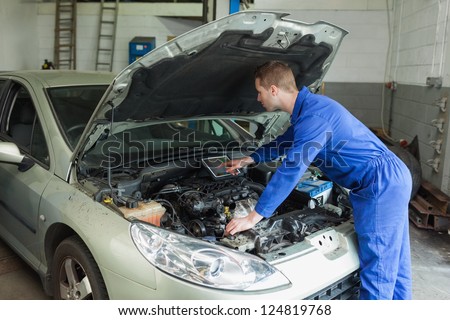 Male mechanic examining car engine with the help of digital tablet