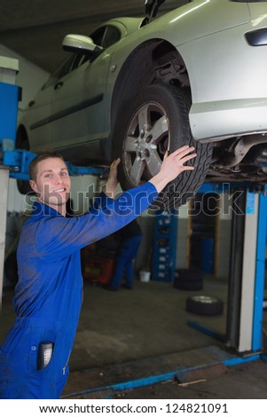 Car on hydraulic lift as mechanic examining tire in garage