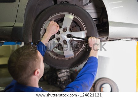 Rear view of male mechanic fixing car tire