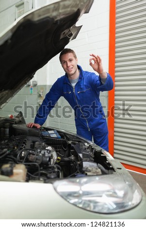 Portrait of young male mechanic by car making ok sign