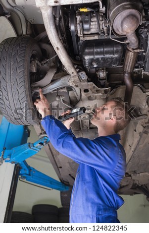 Side view of auto mechanic with flashlight examining under car
