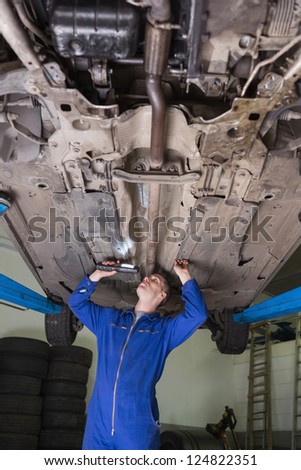 Male auto mechanic examining car using flashlight