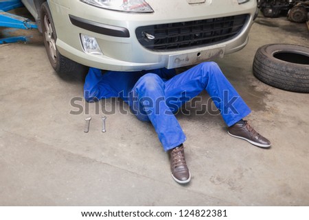 Mechanic working under car in garage