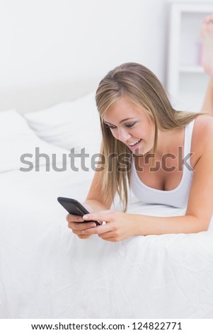 Blonde woman using her phone lying on the bed in the bedroom