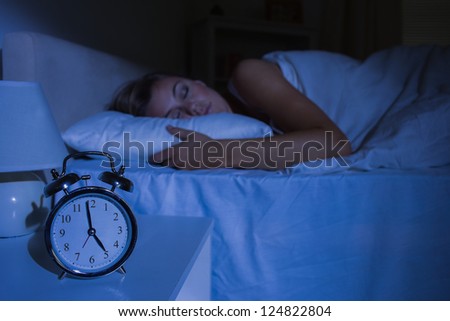 Focus on the alarm clock in front of sleeping woman at night in the bedroom