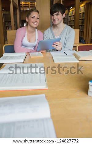 Smiling students with tablet pc at study table in college library