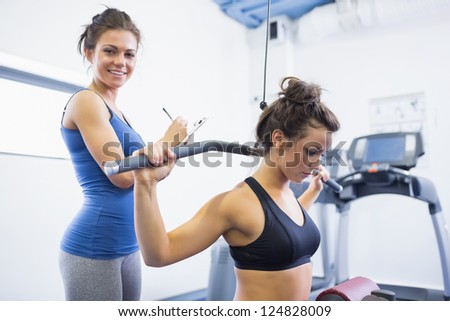 Smiling trainer with woman using weights machine in gym