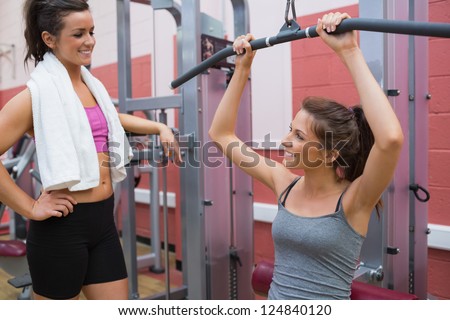 Woman talks to friend using weight machine in gym