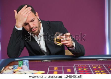 Man looking at whiskey glass at roulette table