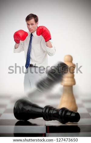 Businessman in boxing gloves knocking over chess pieces on a chessboard