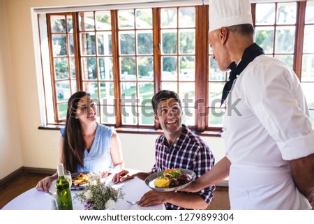 Male chef serving food to young couple sitting in a restaurant