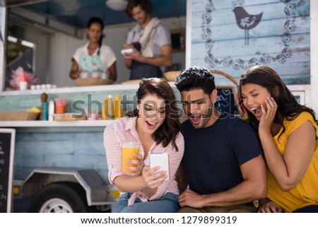 Smiling friends using mobile phone at food truck van